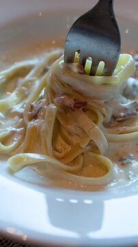 Fork Twirling Creamy Fettuccine Carbonara Pasta in a White Bowl
