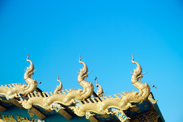 Fototapeta premium Gold naga patterns decorative on roof Thai temple on bright blue sky background