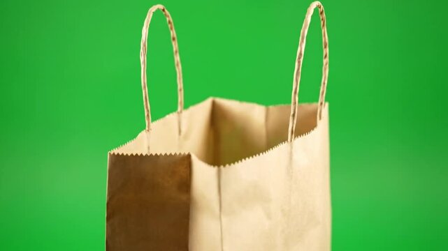 Empty brown paper shopping bag with handles opening and closing against vibrant green backdrop