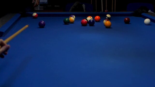 Person playing pool on blue table with colorful balls and cue stick