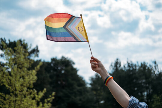 Hand holding intersex inclusive progress pride flag waves against cloudy sky. Symbolic LGBTQ accessories, celebrating identity outdoors, summer pride events.