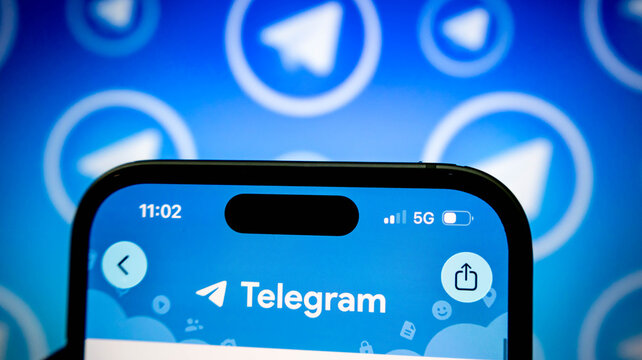Closeup of a smartphone screen displaying the telegram messaging app logo with a blurred background of the telegram icon pattern
