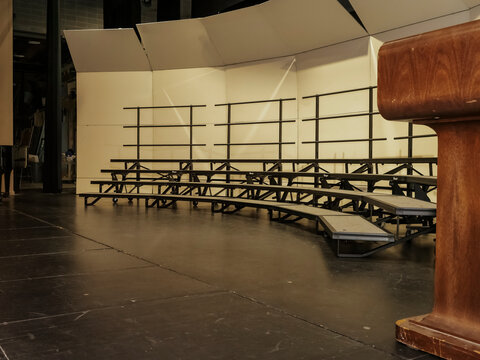 An empty dark performance stage equipped with metallic choir risers portable tiered step platforms and a wooden podium presentation lectern
