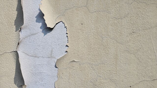 The walls whose paint is peeling off because they are old and exposed to heat and rain, the wall paint is yellow. Abstract background texture from a wall with damaged paint.