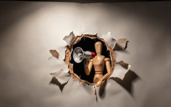 Wooden man with megaphone announces through torn paper hole