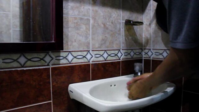 video of a man washing his hands and drinking water from the faucet in his bathroom at home