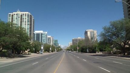 Obraz premium Wide city street lined with modern high-rise buildings and trees under a clear blue sky