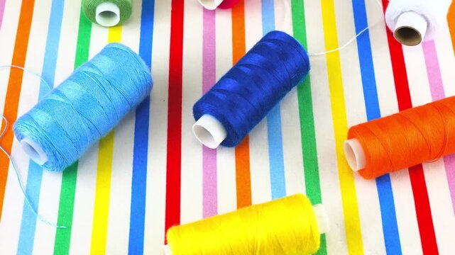 Colorful sewing thread spools on striped textile background top view.