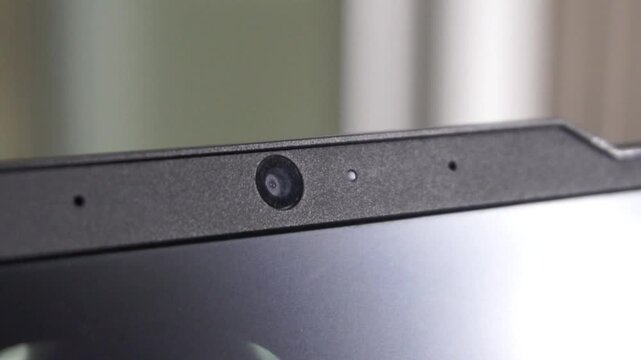 Close up of a built-in webcam on a modern black laptop bezel. Concept for cyber security, internet privacy, digital surveillance, and video conferencing technology in a home office setting.