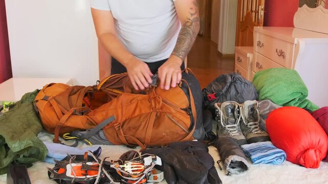 Man unpacking hiking backpack on bed, pulling out mountain gear and clothing after outdoor trek, sorting camping equipment and travel items at home after returning from alpine adventure trip.