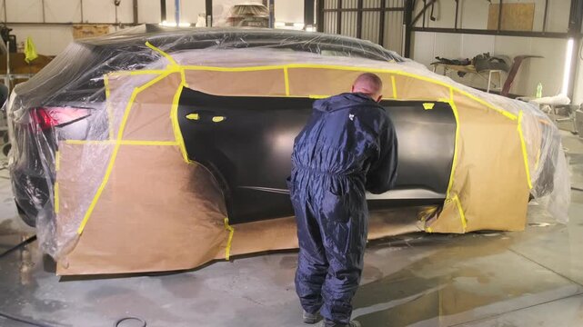 Auto body painter inspecting fresh paint and clear coat with inspection light on repaired car panel in workshop, checking coating quality after collision refinishing and lacquer application