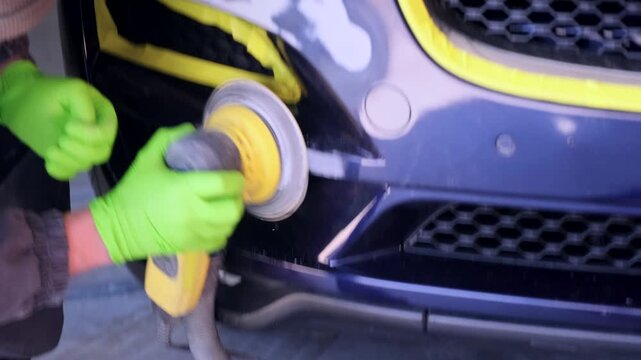 Auto technician smoothing repaired bumper section with polishing tool in collision garage close-up, preparing damaged panel for repainting after traffic accident