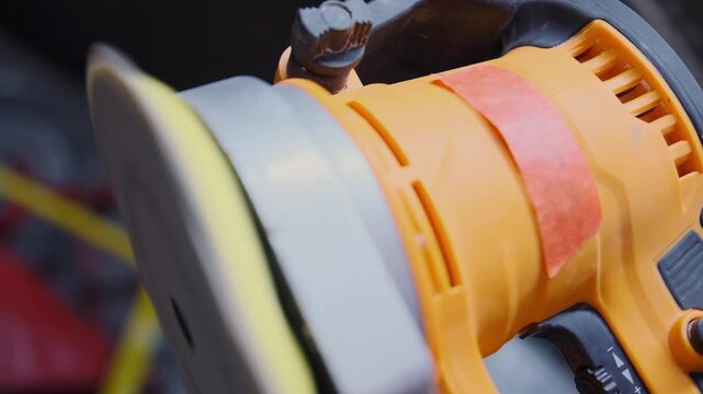 Electric orbital sander polishing surface in close-up during renovation work, professional power tool for woodworking, construction finishing and repair tasks. The orbital sander machine is working.