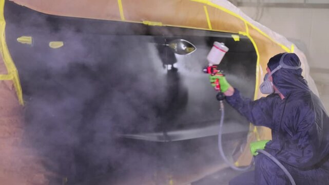 Auto body painter spraying clear coat on repaired car door in workshop, applying lacquer over fresh paint during collision restoration, refinishing service and insured vehicle repair.