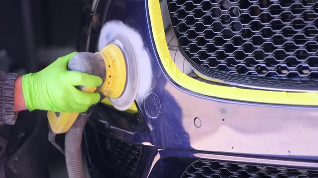 Technician buffing front grille area with rotary polisher in auto collision workshop close-up, restoring paint coating after accident damage and claim processing