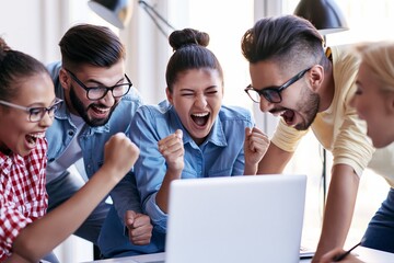 Fototapeta premium Excited young coworkers celebrating success around laptop