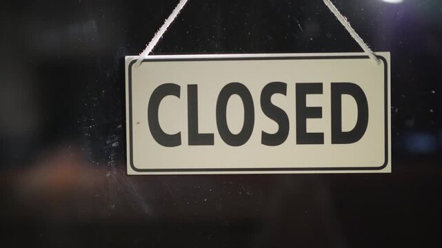 Close up on a white sign with the word closed in bold black letters hanging on glass.