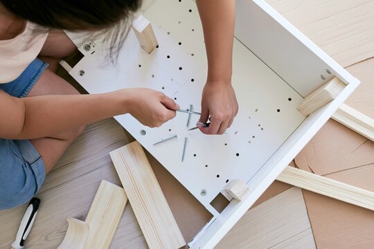Woman assembling cabinet with screwdriver and wooden panels
