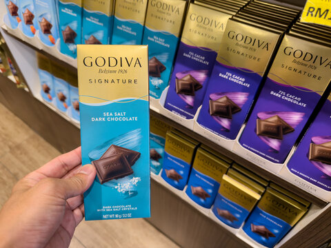 LANGKAWI, MALAYSIA - MAR 18, 2026: Hand holding a Godiva Signature Sea Salt Dark Chocolate bar in a retail store.