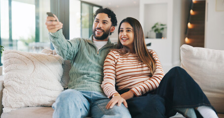 Obraz premium Happy couple, watching tv and people with remote in lounge, bonding and streaming movie with partner. Love, man and woman with smile for film, entertainment or channel change with controller in house