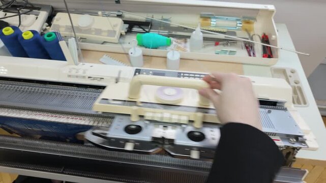 Top down view of a knitting workstation, including multiple spools of yarn, thread guides, and machine controls