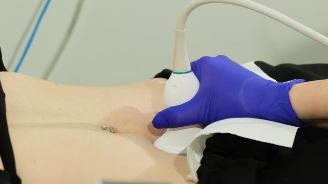 Doctor hand uses probe to exam patient pelvis with belly button piercing in clinic slow motion. Gynecologist researches woman organs with sonograph