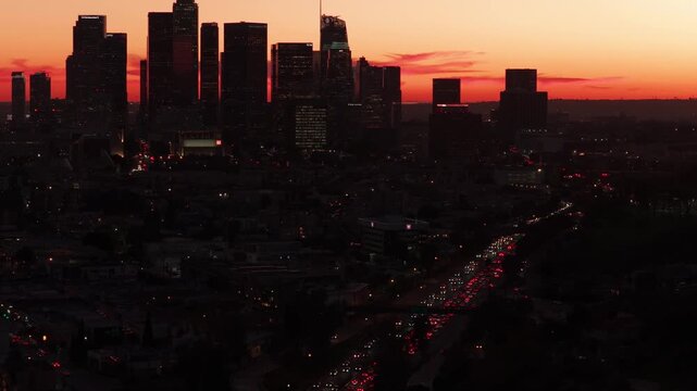Dramatic aerial view of downtown Los Angeles at sunset with city lights and freeway traffic in motion.