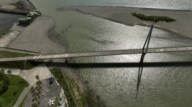Aerial view of Anaklia resort in Georgia featuring the futuristic observation tower, pedestrian bridge over Enguri river, sandy beach, and Black Sea coastline on a sunny day.