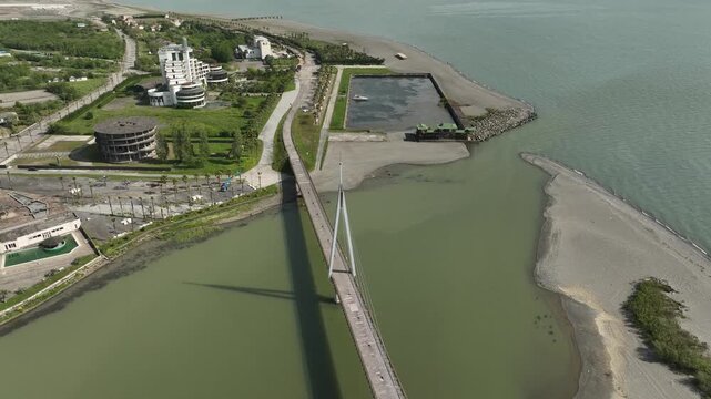 Aerial view of Anaklia resort in Georgia featuring the futuristic observation tower, pedestrian bridge over Enguri river, sandy beach, and Black Sea coastline on a sunny day.
