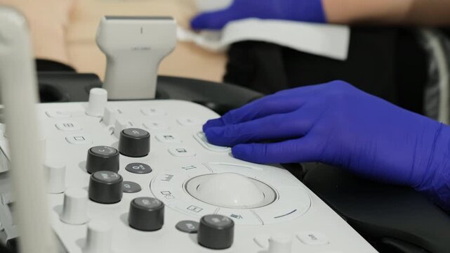 Gloved hand works over ultrasound console during gynecology procedure. Specialist adjusts controls calibrating scan while guiding diagnosis