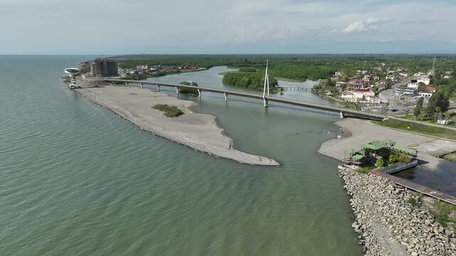 Aerial view of Anaklia resort in Georgia featuring the futuristic observation tower, pedestrian bridge over Enguri river, sandy beach, and Black Sea coastline on a sunny day.