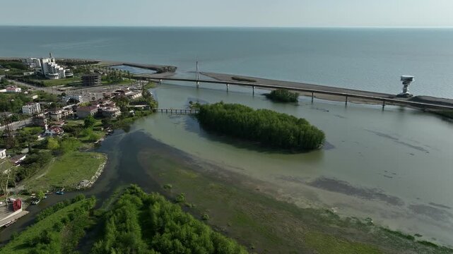 Aerial view of Anaklia resort in Georgia featuring the futuristic observation tower, pedestrian bridge over Enguri river, sandy beach, and Black Sea coastline on a sunny day.