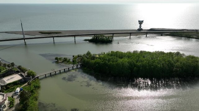 Aerial view of Anaklia resort in Georgia featuring the futuristic observation tower, pedestrian bridge over Enguri river, sandy beach, and Black Sea coastline on a sunny day.
