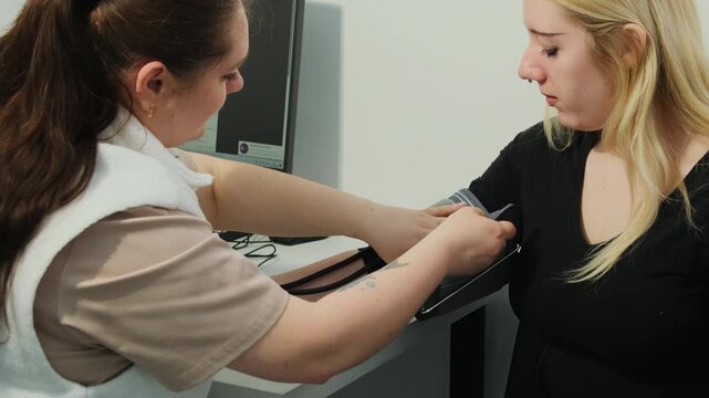 Doctor puts blood pressure monitor cuff onto young woman arm in clinic. Skilled nurse examines female patient with medical tool in hospital slow motion