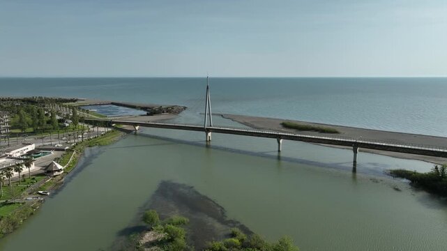 Aerial view of Anaklia resort in Georgia featuring the futuristic observation tower, pedestrian bridge over Enguri river, sandy beach, and Black Sea coastline on a sunny day.