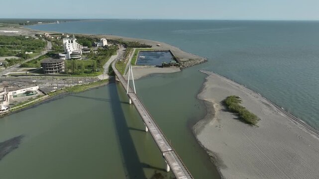 Aerial view of Anaklia resort in Georgia featuring the futuristic observation tower, pedestrian bridge over Enguri river, sandy beach, and Black Sea coastline on a sunny day.