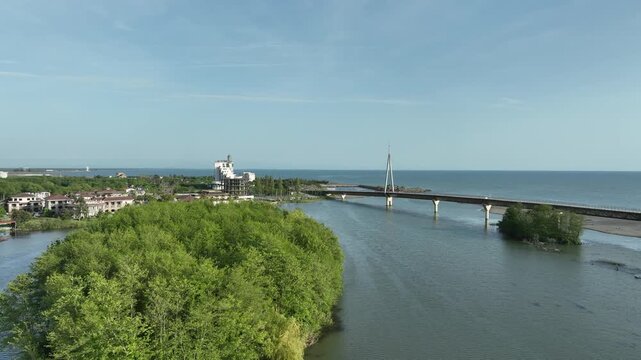 Aerial view of Anaklia resort in Georgia featuring the futuristic observation tower, pedestrian bridge over Enguri river, sandy beach, and Black Sea coastline on a sunny day.