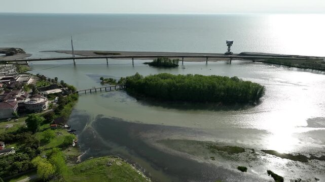 Aerial view of Anaklia resort in Georgia featuring the futuristic observation tower, pedestrian bridge over Enguri river, sandy beach, and Black Sea coastline on a sunny day.