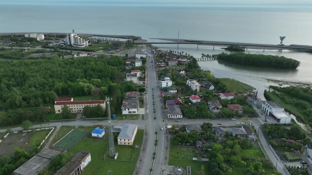 Aerial view of Anaklia resort in Georgia featuring the futuristic observation tower, pedestrian bridge over Enguri river, sandy beach, and Black Sea coastline on a sunny day.