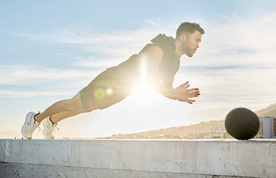 Athlete, man and push up with medicine ball outdoor for fitness, cardio exercise and power training. Male person, clap and equipment for bodybuilding on roof, strength workout and endurance challenge