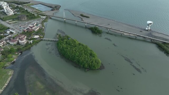 Aerial view of Anaklia resort in Georgia featuring the futuristic observation tower, pedestrian bridge over Enguri river, sandy beach, and Black Sea coastline on a sunny day.
