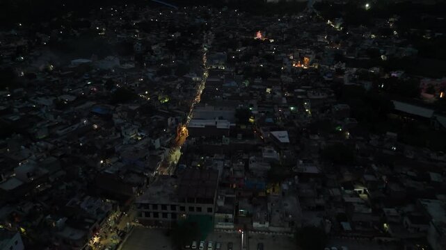 Aerial view of the narrow local roads, moving traffic, and glowing streetlights in Barsana city at night.