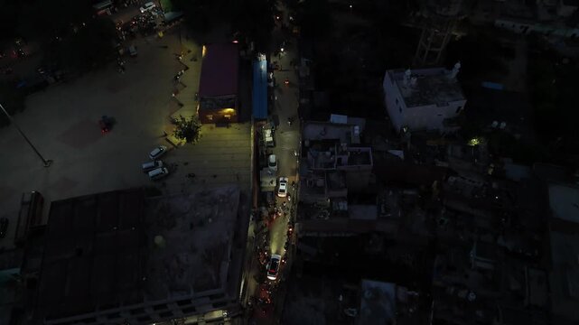 Aerial view of the narrow local roads, moving traffic, and glowing streetlights in Barsana city at night.