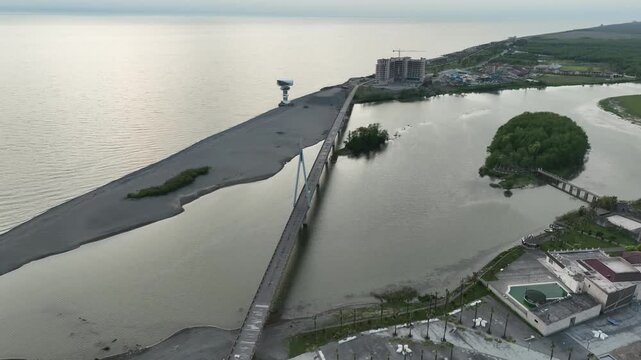 Aerial view of Anaklia resort in Georgia featuring the futuristic observation tower, pedestrian bridge over Enguri river, sandy beach, and Black Sea coastline on a sunny day.