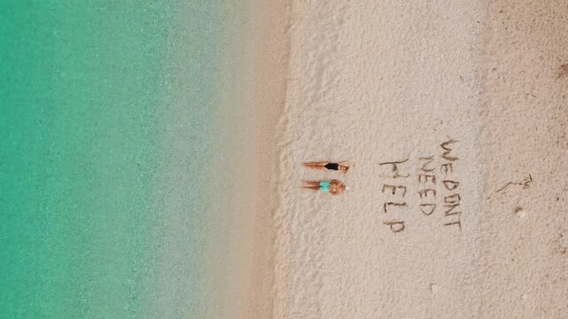 Couple relax on remote turquoise beach beside playful We dont need help sand message