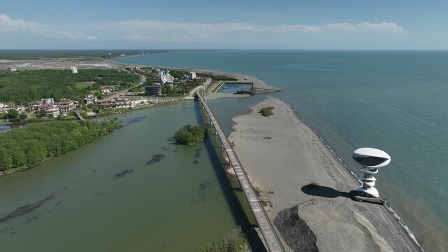 Aerial view of Anaklia resort in Georgia featuring the futuristic observation tower, pedestrian bridge over Enguri river, sandy beach, and Black Sea coastline on a sunny day.