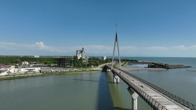 Aerial view of Anaklia resort in Georgia featuring the futuristic observation tower, pedestrian bridge over Enguri river, sandy beach, and Black Sea coastline on a sunny day.
