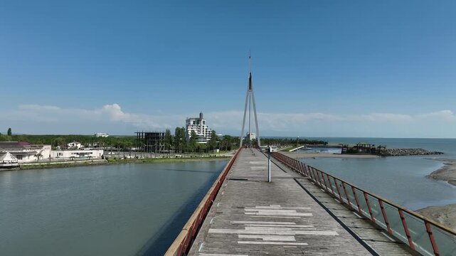 Aerial view of Anaklia resort in Georgia featuring the futuristic observation tower, pedestrian bridge over Enguri river, sandy beach, and Black Sea coastline on a sunny day.