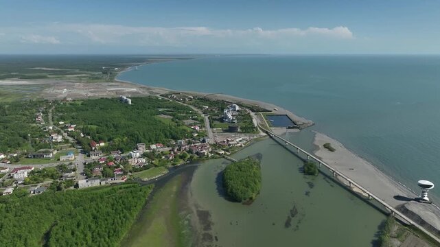 Aerial view of Anaklia resort in Georgia featuring the futuristic observation tower, pedestrian bridge over Enguri river, sandy beach, and Black Sea coastline on a sunny day.