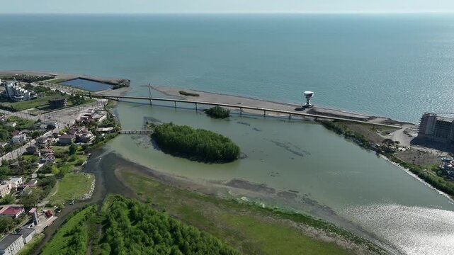 Aerial view of Anaklia resort in Georgia featuring the futuristic observation tower, pedestrian bridge over Enguri river, sandy beach, and Black Sea coastline on a sunny day.